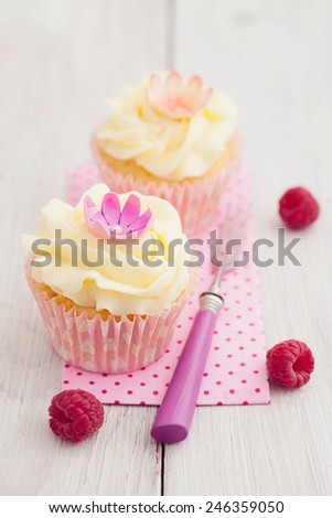 Two purple cupcakes with buttercream frosting swirl, raspberries and edible flowers
