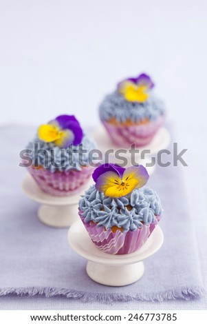 Three mini cupcakes with buttercream topping and edible pansies