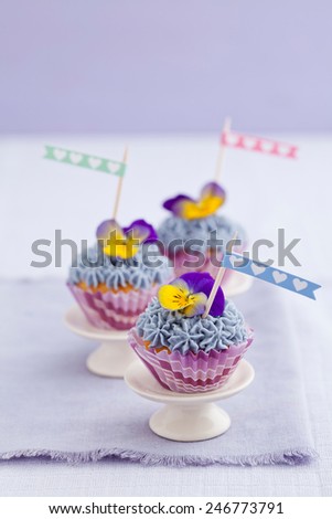 Three mini cupcakes with buttercream topping and edible pansies