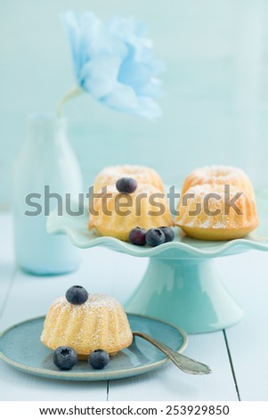 Mini bundt cakes with icing sugar on a cake stand with blueberries and a paper flower