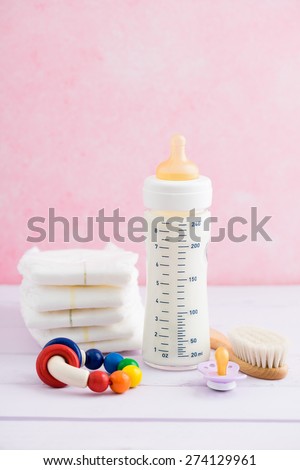 Baby bottle, pacifier, hairbrush, diapers and rattle on pink table