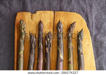 Fresh purple asparagus on vintage wooden baord on linen in dark moody light