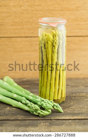 Preserved green asparagus in a glass and fresh green asparagus on wooden table
