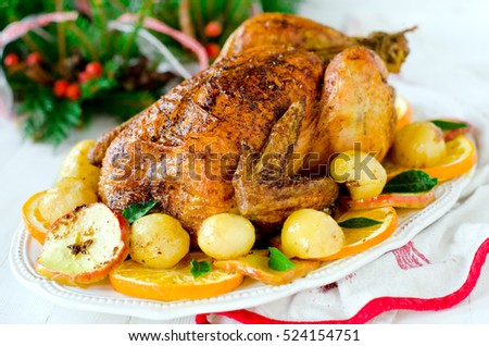 Christmas baked chicken (turkey) with oranges and apples on a white table with Christmas decorations