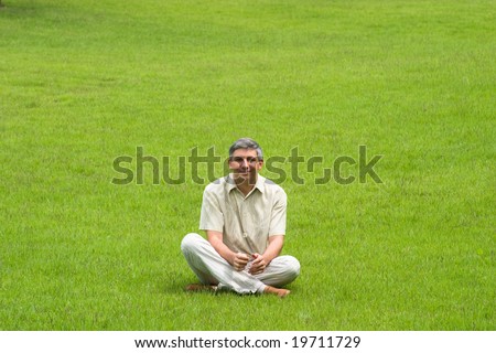 Smiling man with crossed legs sitting on grass field
