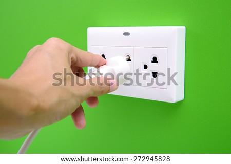 Electric power plug in a hand and inserting into power wall socket