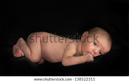 An alert naked newborn baby lying on black background