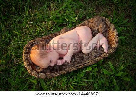 An alert newborn baby lies in basket in grass