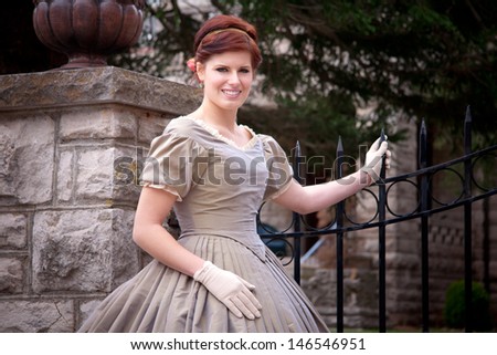 An elegant woman wearing a Civil War era ball gown stands by a stone and wrought iron gate