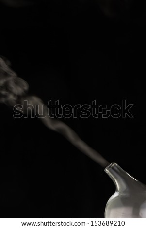 Vapor, smoke, or essential oil emitting from a glass nebulizer on a black background