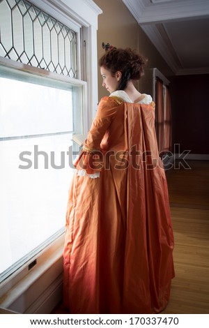 A young woman in historical clothing in the window of an 18th century mansion