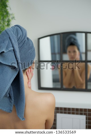 woman with towel on her head looks into mirror