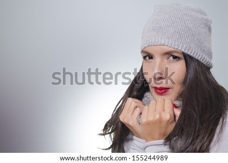 Pretty young woman in winter fashion cuddling down inside her grey woolly knitted jersey, scarf and cap on a cold day with copyspace