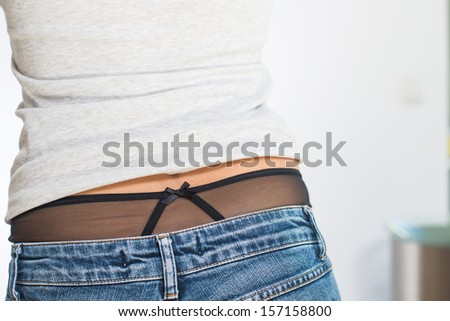View from behind of a shapely woman in jeans wearing black panties which are visible where her t-shirt has creased and rucked up her back to expose her midriff
