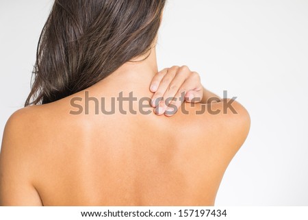 Woman with upper back and neck pain standing naked with her back to the camera and her hand rubbing her shoulder muscles close to the spine Woman with upper back and neck pain standing naked with her back to the camera and her hand rubbing her shoulder muscles close to the spine