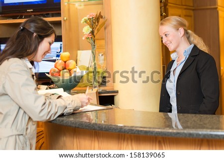 Young woman checking in at the hotel reception with friendly receptionist
