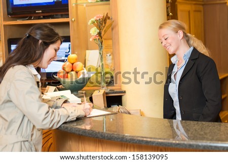 Young woman checking in at the hotel reception with friendly receptionist