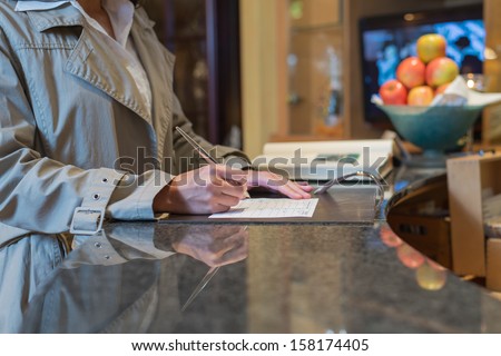 female hotel guest filling in registration form upon checking in, service and tourism concept
