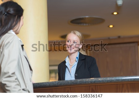 Beautiful friendly smiling receptionist behind the service desk in a hotel lobby helping an attractive female guest indicating with her hand the way to her accommodation