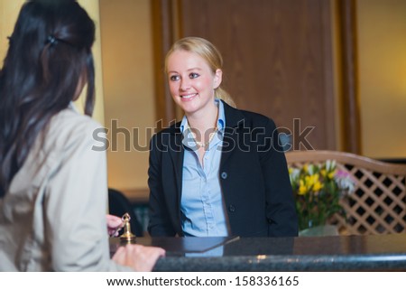 Beautiful Friendly Smiling Receptionist Behind The Service Desk In A Hotel Lobby Helping An Attractive Female Guest Indicating With Her Hand The Way To Her Accommodation