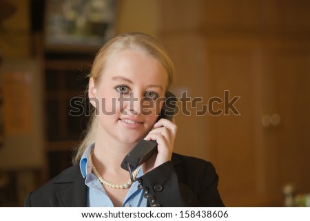Beautiful blond woman wearing a suit answering an office telephone at work