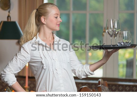 Elegant beautiful young woman serving drinks gracefully balancing the tray with glasses of white wine on her fingertips standing in profile with a friendly smile