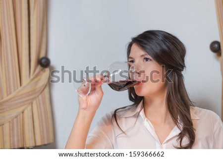 Attractive young brunette woman drinking a glass of red wine and looking away to the left of the camera