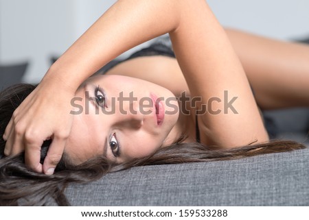 Beautiful appealing young woman lying on her back in seductive lingerie looking back at the camera with a serious wide eyed expressiong