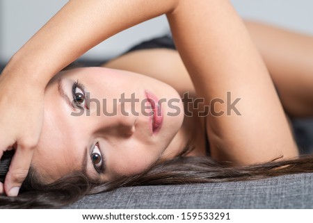 Beautiful appealing young woman lying on her back in seductive lingerie looking back at the camera with a serious wide eyed expressiong