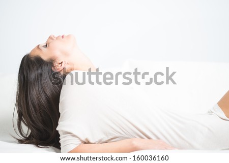 Side view of a beautiful young woman reclining on a sofa with her head tilted back and her long brunette hair dangling down behind her as she relaxes daydreaming at home