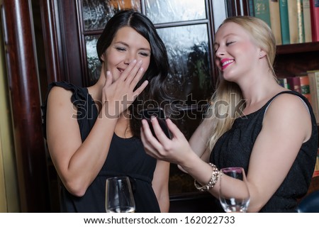 Two stylish beautiful young women in evening wear standing smiling and laughing as they look at a text message on a mobile phone