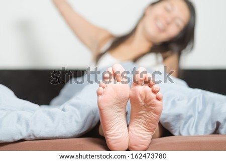Close up of the cute crinkled soles of female feet belonging to a smiling playful woman relaxing in her bed with focus to the feet