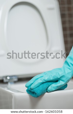 Hand of a person cleaning the toilet seat in rubber gloves with a sponge disinfecting the underside for germs and bacteria while performing household chores