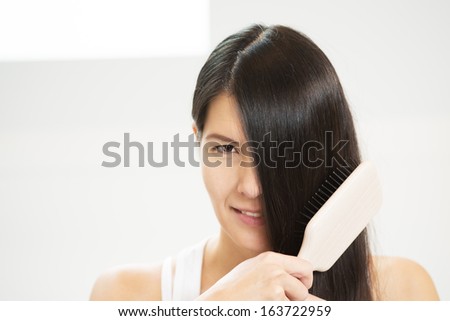 Attractive woman brushing her hair with one eye concealed by her long brunette locks looking at the camera with a sensual seductive look