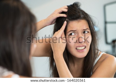 Horrified Young Woman Looking In The Bathroom Mirror Staring Open Mouthed At The First Grey Hair On Her Scalp, A First Sign Of Aging, Or Noticing That She Is Suffering From Dandruff