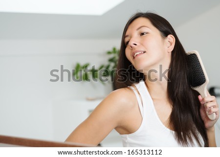 Attractive woman brushing her hair looking at the camera with a friendly charming smile