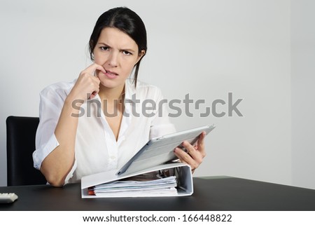 Puzzled woman thinking hard and grimacing as she tries to find an answer to a problem posed on her handheld tablet computer