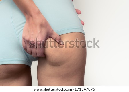 Slender young woman checking for excess weight on her buttocks pinching the muscle between her hands, closeup view of her hand