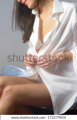 Young woman unbuttoning her white shirt as she prepares to go to bed in the evening with a tantalizing glimpse of her bra visible