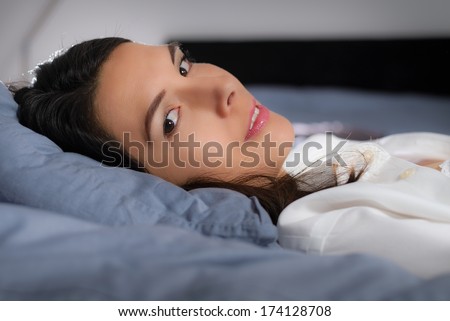 Low angle closeup view of a refreshed young woman resting in bed lying back on her pillow turning her head to look at the camera