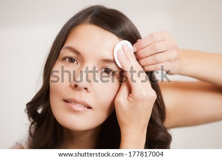 Beautiful topless young woman with long brunette hair carefully cleaning her skin with a cotton pad in the morning during her daily cleansing routine and skin care