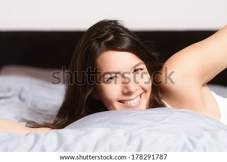 Healthy woman refreshed after a good nights sleep stretching in bed and smiling at the camera in pleasure and satisfaction