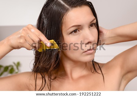 Woman combing out lice in her hair with a lice comb grimacing as she pulls the fine teeth through her long brown tresses to control the contagious infestation of tiny wingless insects