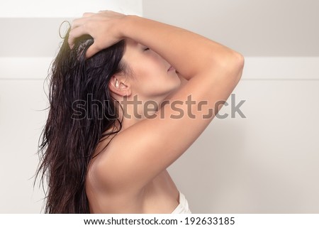 Attractive serious young woman standing in her bathroom with bare shoulders shampooing her long brown hair massaging her scalp with her fingers