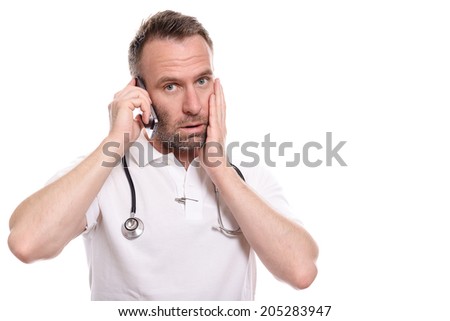 Middle-aged male doctor in a white shirt and stethoscope taking a call on his mobile phone with a worried expression as he listens to the conversation, isolated on white