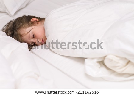 Cute little girl fast asleep in bed rolled up warmly in a white duvet with a serene expression as she dreams sweet dreams