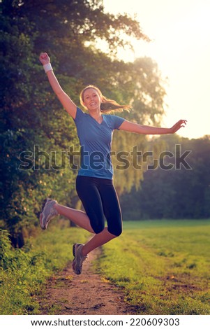 Energetic woman leaping in the air with a happy smile full of vitality as she runs along a country track during a physical workout and training