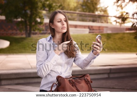 Young woman refreshing her hairstyle in an urban street watching herself in a small handheld mirror as she combs her long brown hair