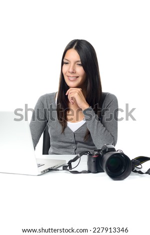 Attractive female photographer sitting back in her chair smiling in satisfaction at her captures as she looks at the screen of her laptop with her camera nearby
