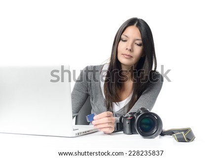 Serious Young female Photographer Transferring Image Files From SD Card to Laptop at her Desk. Isolated on White Background.